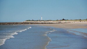 A beach with a lighthouse, rocky shoreline, and a sandy area with people. - Beach front home in Blåvand with sauna (Blåvand)