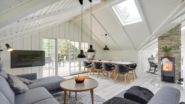 A spacious living room with a high ceiling, a dining area with a long table and chairs, and a stone wall. - Beach front home in Blåvand with sauna (Blåvand)