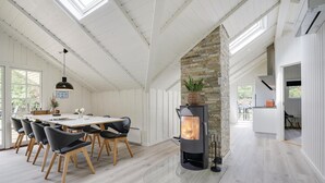 A modern kitchen with a stone fireplace, wooden dining table, and black chairs. - Beach front home in Blåvand with sauna (Blåvand)