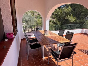 Une terrasse avec une table et des chaises en bois, un panier rose et un barbecue.