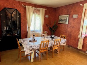 A dining room with a table set for four, wooden chairs, a cabinet with glass doors, and a window with curtains.