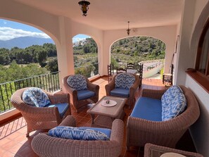 A balcony with wicker furniture and a view of a mountainous landscape.