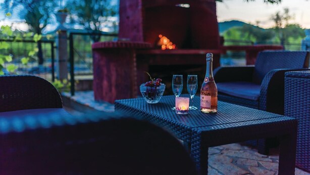 Une terrasse avec des meubles en osier, une bouteille de vin et des verres sur une table.