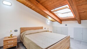 A bedroom with a wooden ceiling and skylight, a bed, a bedside table, and a wardrobe.