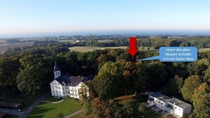 An aerial view of a property with a large white building surrounded by trees and fields. A red arrow points to a smaller building labeled as a sauna house. - Holiday in the castle park Hohen Niendorf with terrace & view to the Baltic Sea (Hohen Niendorf)