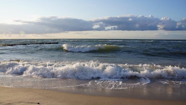 A beach with waves crashing onto the shore and a cloudy sky. - Holiday in the castle park Hohen Niendorf with terrace & view to the Baltic Sea (Hohen Niendorf)