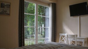 A bedroom with a large window, a bed, a desk, and a TV. - Holiday in the castle park Hohen Niendorf with terrace & view to the Baltic Sea (Hohen Niendorf)