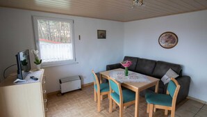 Um quarto com uma escrivaninha de madeira, uma mesa com cadeiras, um sofá, um radiador, uma janela e um ventilador de teto.