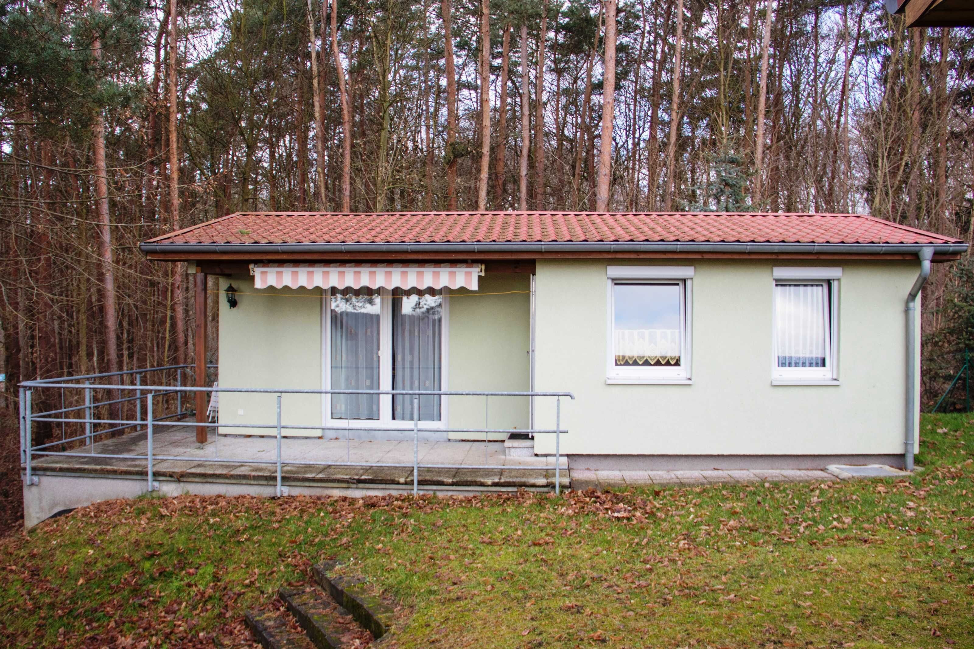 Un piccolo edificio a un piano con tetto in tegole, un portico con ringhiera e una finestra con tenda.