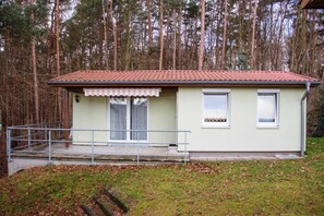 Um pequeno edifício térreo com telhado de cerâmica, varanda frontal com guarda-corpo e janela com cortina.