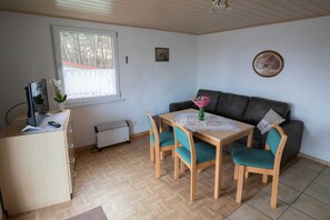 A room with a wooden desk, a table with chairs, a sofa, a radiator, a window, and a ceiling fan. - Holiday home Charlotte - Holiday home Reinhold in Feldberg (Feldberger Seenlandschaft)