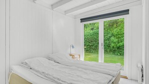 Ein Schlafzimmer mit einem Bett, einem Schreibtisch und einem Fenster mit Blick auf Grün.