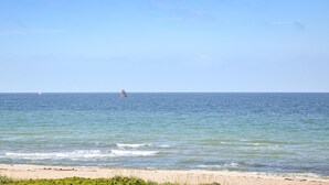 Ein Strand mit ruhigem Wasser und einem entfernten Segelboot.