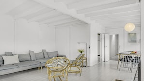 Ein modernes Wohnzimmer mit grauem Sofa, Korbstühlen, einem Esstisch mit Stühlen und einer Pendelleuchte.