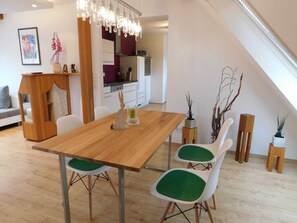 A dining area with a wooden table and green cushioned chairs, a chandelier, and a kitchen in the background. - Trudis Apartment - Apartment 5 ***** (DG) (Veringenstadt)