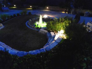 Un jardín ajardinado con una fuente, escalones de piedra y una zona de césped circular.