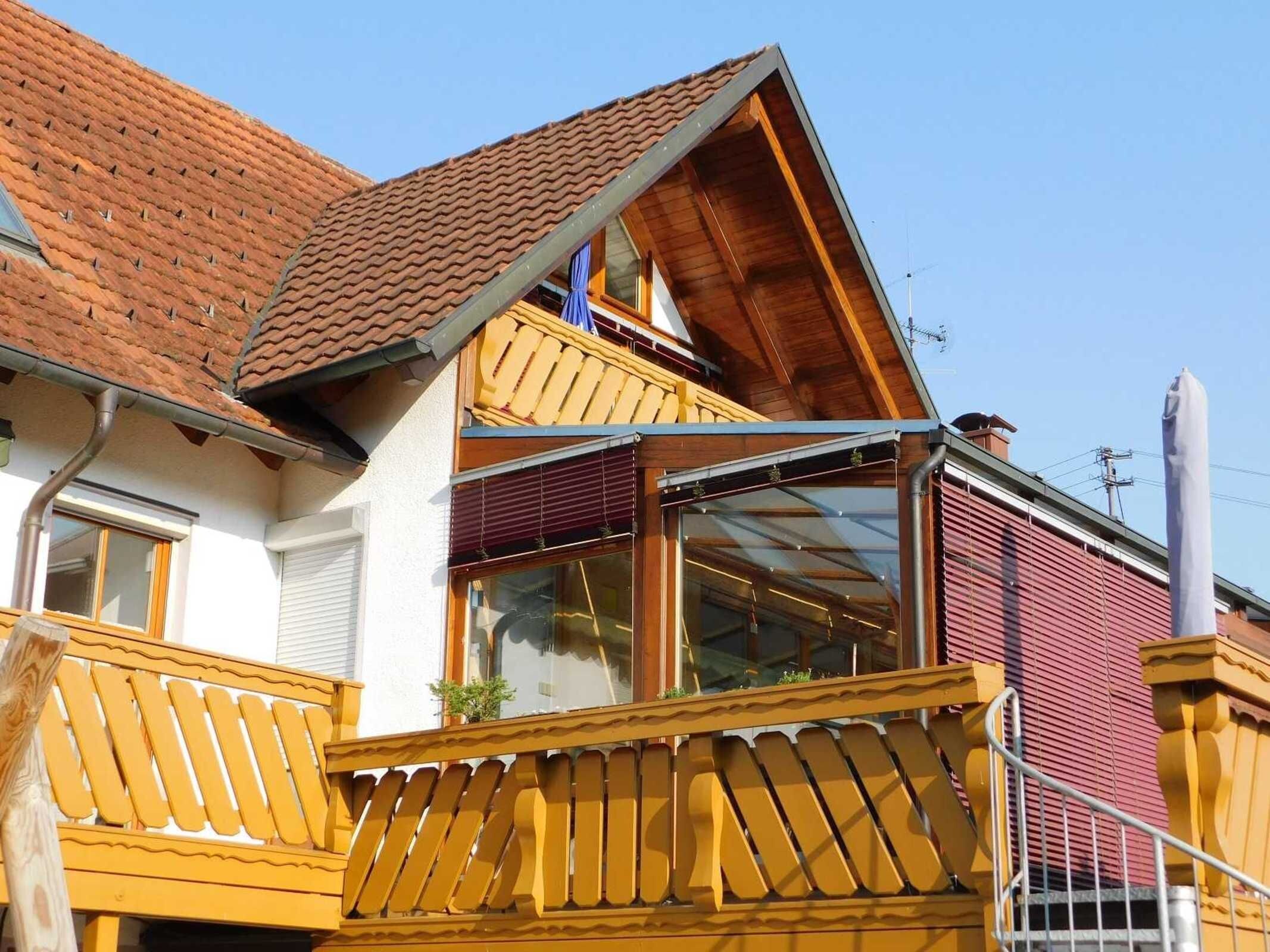 Ein zweistöckiges Haus mit rotem Ziegeldach, einem Balkon mit gelben Geländern und einem großen Fenster.