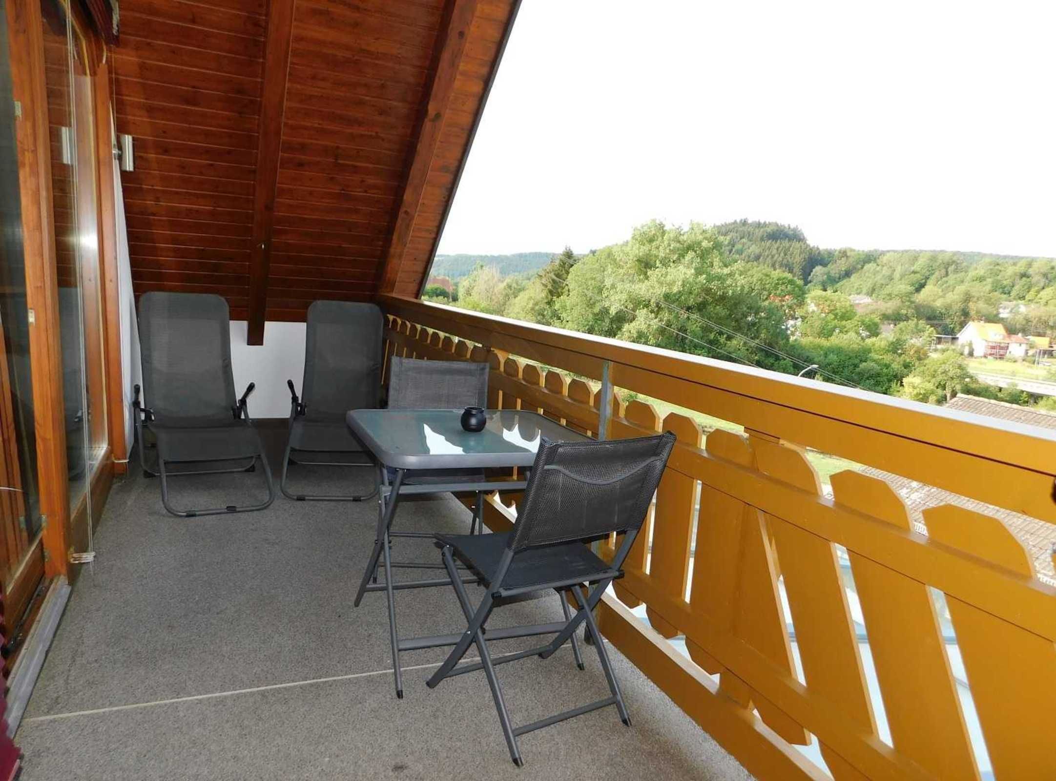 Ein Balkon mit Tisch und zwei Stühlen, Blick auf eine bewaldete Landschaft und Holzboden.