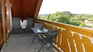 Ein Balkon mit Tisch und zwei Stühlen, Blick auf eine bewaldete Landschaft und Holzboden.