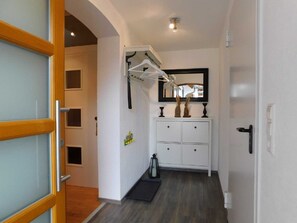 Un pasillo con un armario blanco, un perchero, una mesita con un jarrón y una puerta con marco de madera.