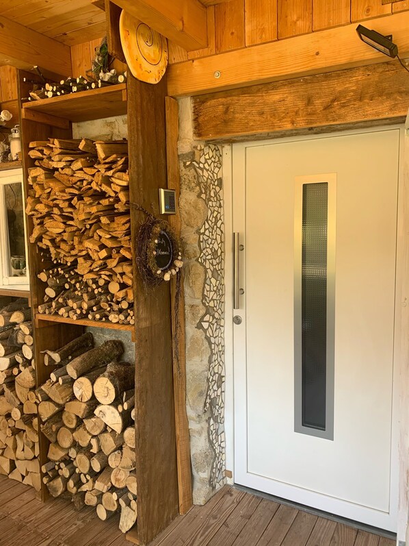 A wooden interior with a white door, a stone wall with mosaic, and shelves with neatly stacked firewood.