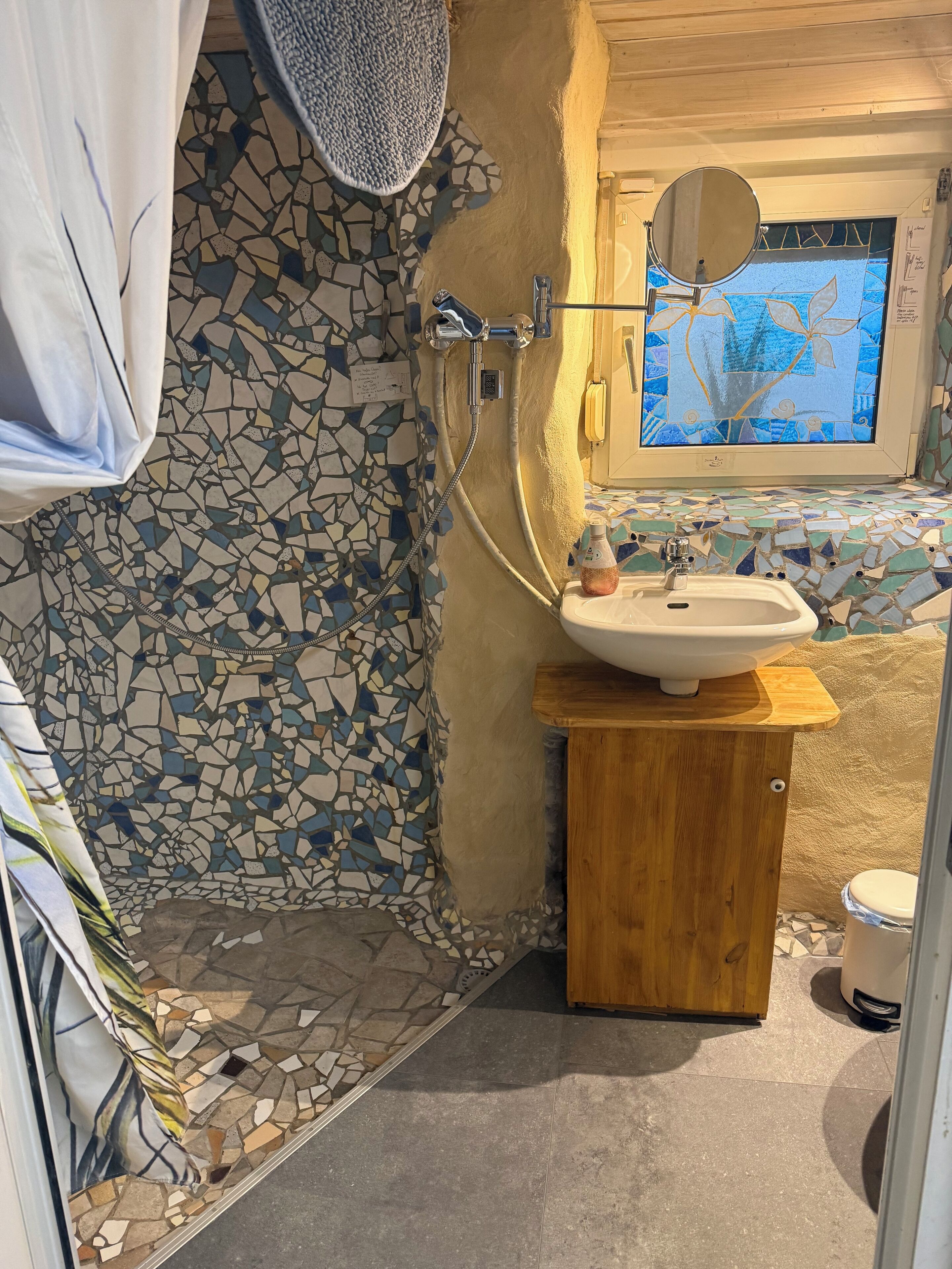 Un bagno con parete doccia in mosaico, un mobile contenitore in legno con lavandino e uno specchio sopra il mobile.
