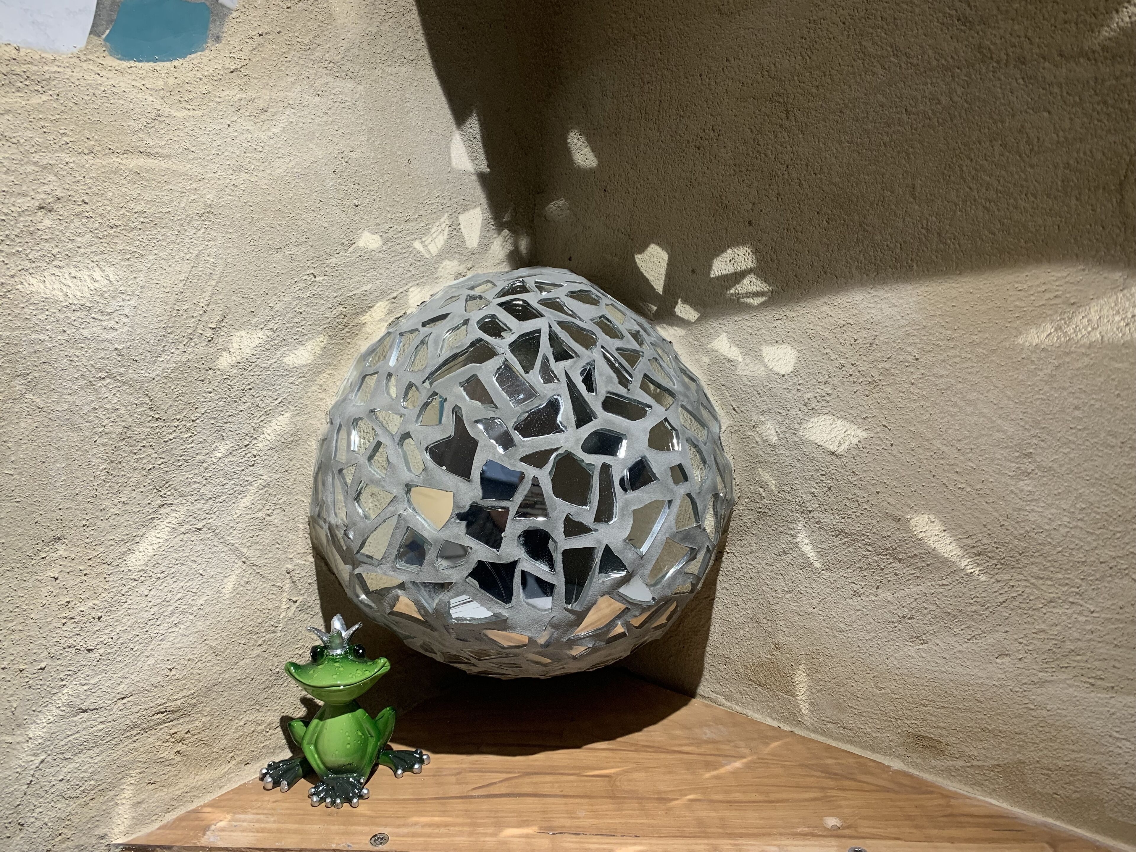 Eine dekorative Glaskugel und eine kleine Froschfigur auf einer Holzoberfläche vor einer strukturierten Wand.