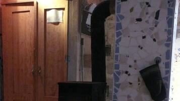 Sobim cuita de llenya amb foc visible, un cubet metàl·lic i una porta de fusta en una habitació amb un rebedor d'àmfores.