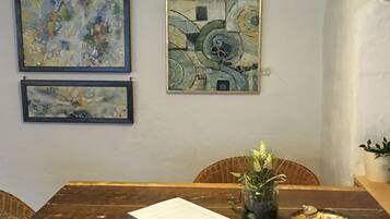 Un comedor con una mesa de madera, dos cuadros abstractos enmarcados, un florero con flores y un bol de bombones.