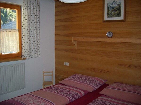Un dormitorio con dos camas, cabeceros de madera, una ventana con cortinas, un radiador y un cuadro en la pared.