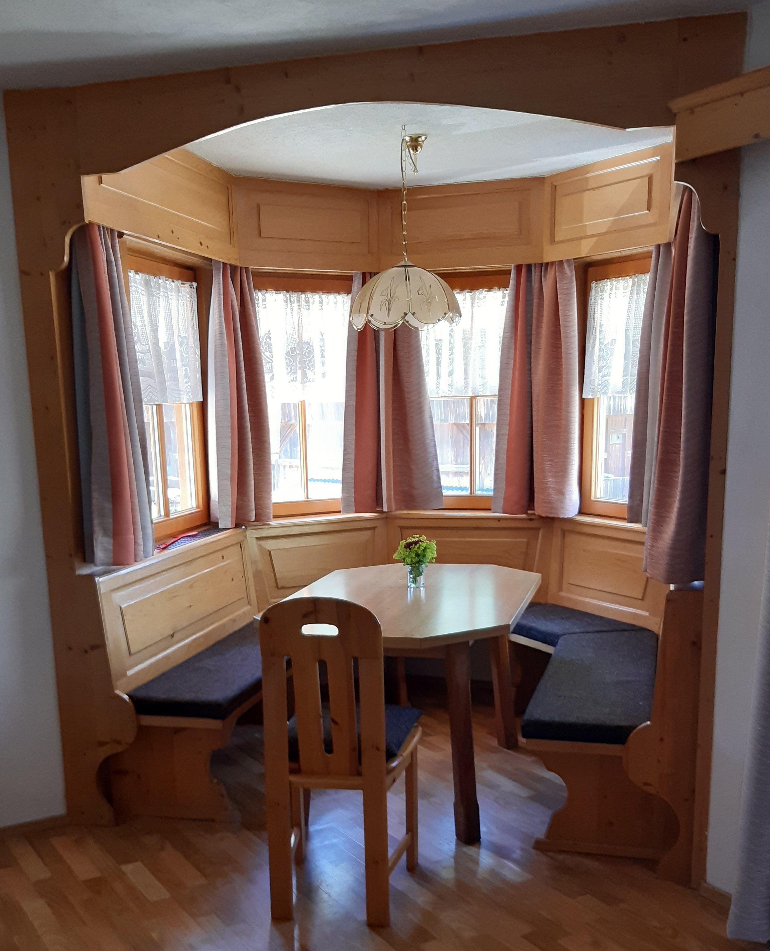 Ett hörnrum med en träbänk som sittplats, ett runt bord och en hängande lampa.