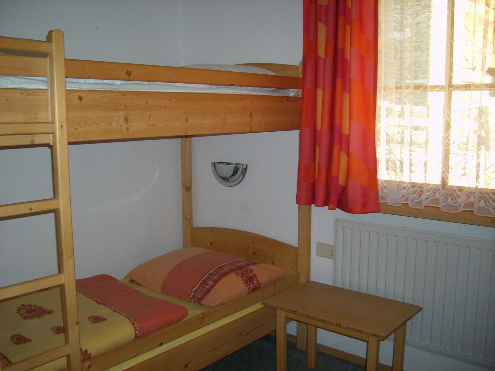 A bunk bed with a small table, a window with curtains, and a radiator.