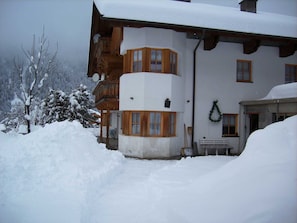 Un edificio cubierto de nieve con balcones de madera, una banca en el exterior y una guirnalda en la pared.