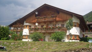 A traditional chalet with wooden balconies, a stone foundation, and a mountainous backdrop. - Fallwindes 1 - Gratzhof - Kals (Lesach)