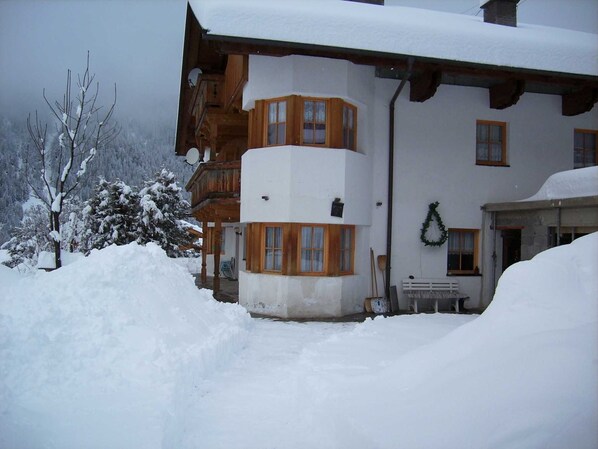 Ein mit Schnee bedecktes Gebäude mit hölzernen Balkonen, einer Bank vor der Tür und einem Kranz an der Wand.