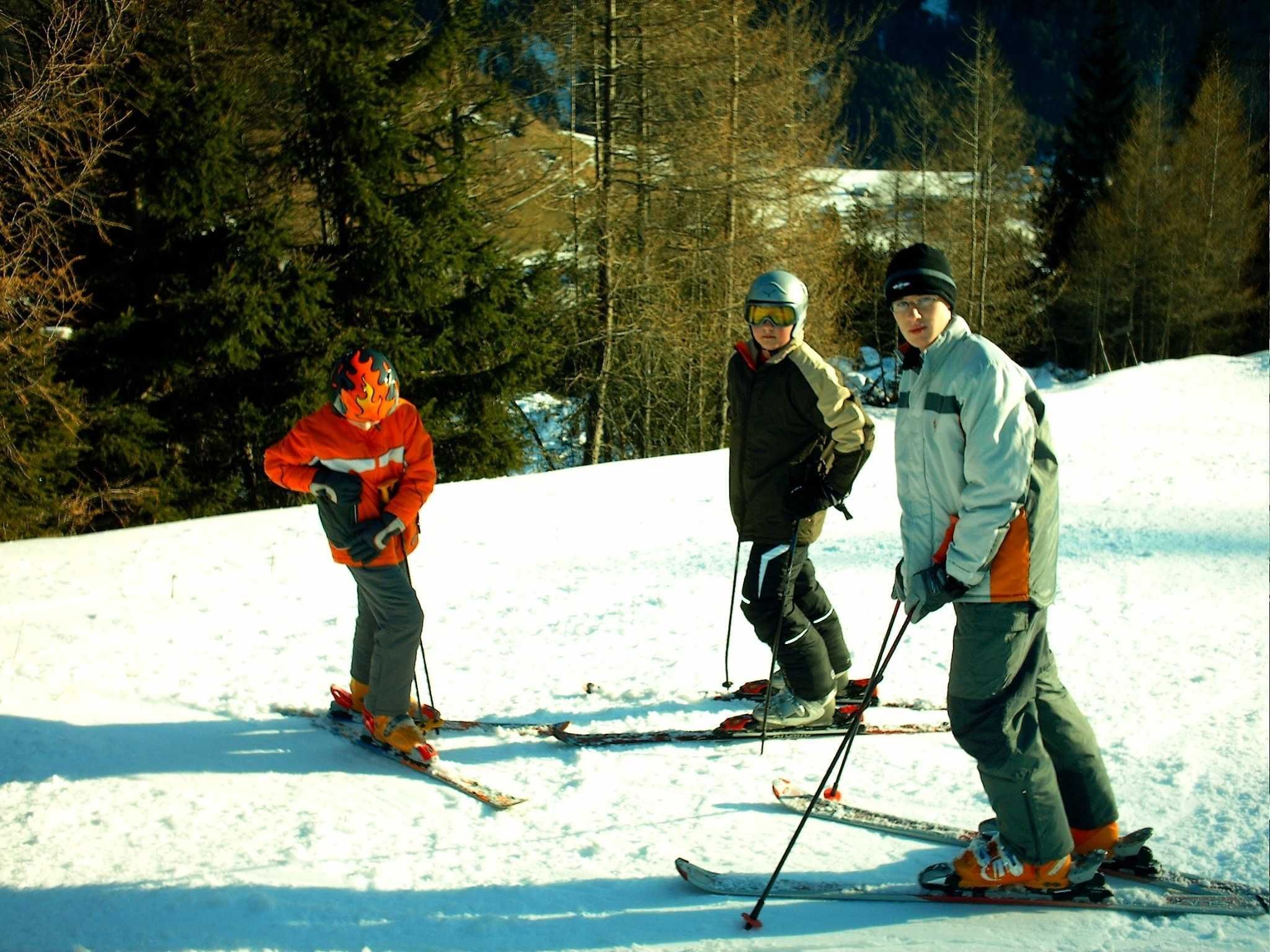 Three people skiing on a snowy slope with trees in the background.