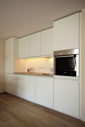 A modern kitchen with white cabinetry, a built-in oven, and a wooden countertop.