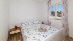 Un dormitorio con cama, mesita de noche, ventana con cortinas y vistas al exterior.