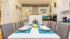 A dining area with a table set for four, a kitchen in the background, and a living area with a sofa and a coffee machine. - Holiday apartment 150 m from the beach (Njivice)