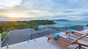 Eine Dachterrasse mit Liegestühlen und Blick auf das Meer und die Hügel.