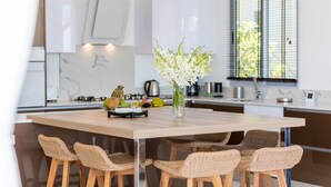 Eine moderne Küche mit einer Holztischinsel, Korbstühlen und einer Vase mit weißen Blumen.