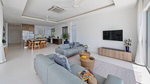 Ein modernes Wohnzimmer mit einer grauen Couch, einem Essbereich mit Holzsesseln und einer Küche im Hintergrund.