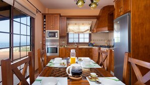 A kitchen with wooden cabinets, a stainless steel refrigerator, a microwave, and a dining table set for breakfast with cups, plates, and a coffee pot. - Finca Vinco with heateble Pool (Alcalá)