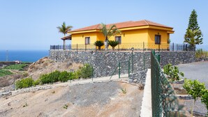 A yellow house with a stone wall foundation, a red-tiled roof, and a view of the ocean. - Finca Vinco with heateble Pool (Alcalá)