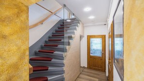 Un escalier moderne avec des rampes en verre et des marches rouges, menant à une porte en bois dotée de panneaux en verre dépoli.