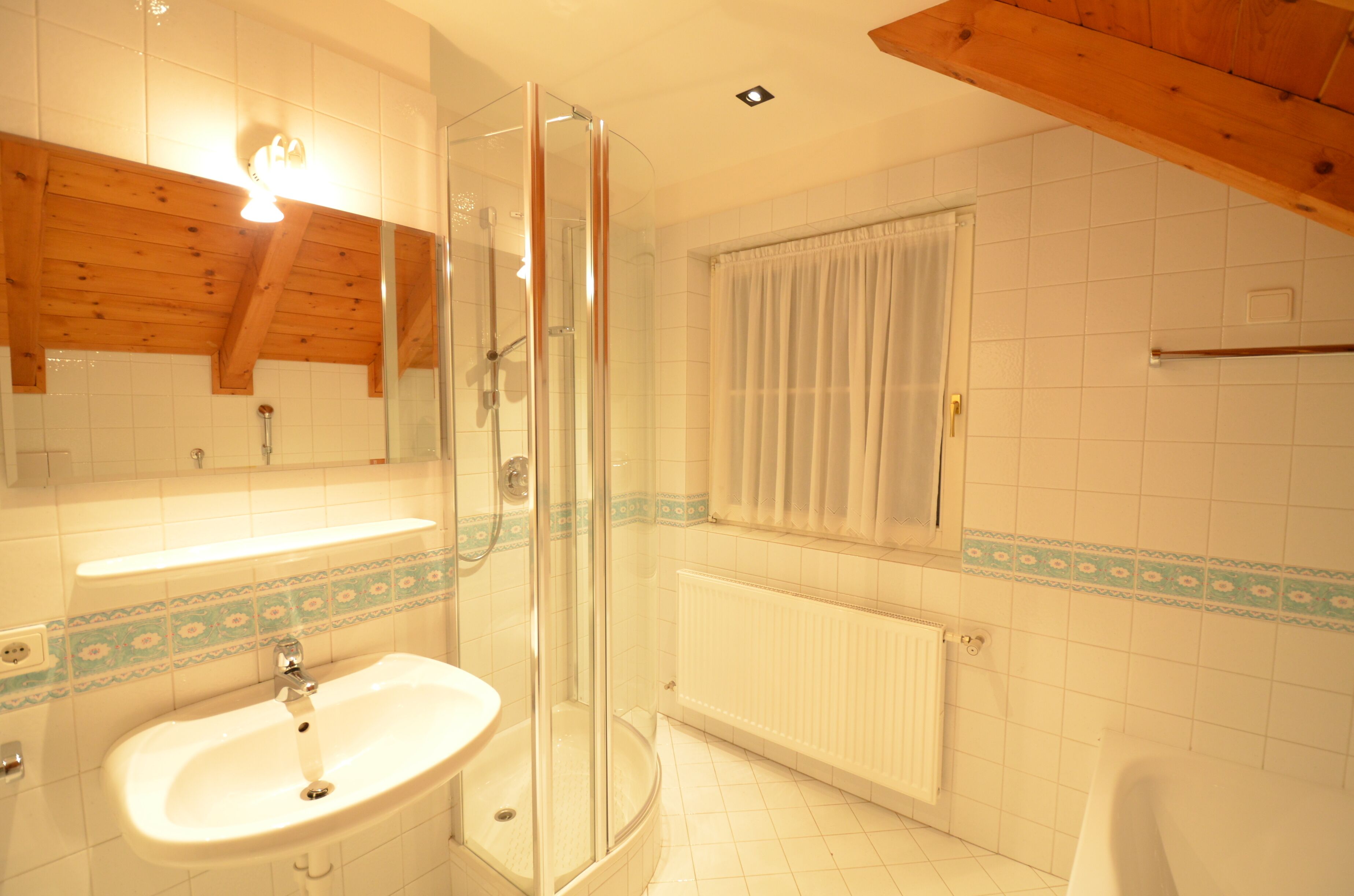 Une salle de bain avec une douche à parois de verre, un lavabo, une fenêtre avec des rideaux et un radiateur.