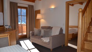 Ein gemütliches Zimmer mit einer Holztreppe, einer Couch, einem Schreibtisch und einem Fenster mit Vorhängen.