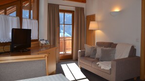 Ein gemütliches Wohnzimmer mit Holzbalkendecke, einer Couch, einem Fernseher und einem Fenster mit Vorhängen.