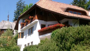 Eine zweistöckige Chalet mit Holzbalkonen und Blumenkästen, umgeben von viel Grün.