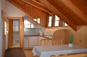Una cocina compacta con vigas de madera, un comedor con mesa y sillas, y vistas al baño contiguo.